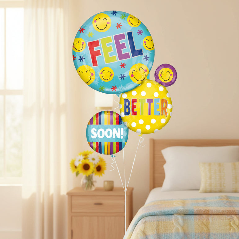 A set of round party balloons with a happy birthday theme, featuring smiley faces, the word 'FEEL' on a light blue balloon, 'BETTER' on a yellow polka-dot balloon, and 'SOON!' on a striped balloon.