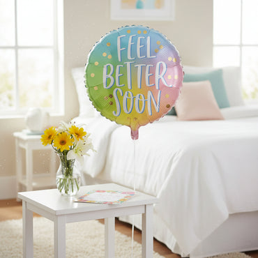 A round foil balloon with a pastel rainbow gradient background and the words 'FEEL BETTER SOON' in large white script with a light blue outline. Small gold confetti dots are scattered across the balloon, and the balloon is shown on a plain white background.