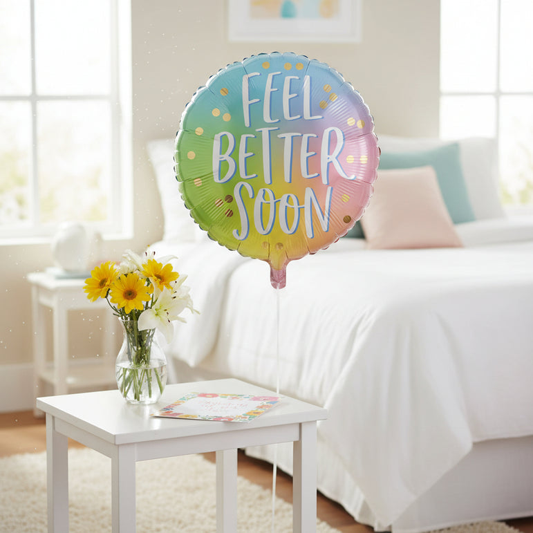 A round foil balloon with a pastel rainbow gradient background and the words 'FEEL BETTER SOON' in large white script with a light blue outline. Small gold confetti dots are scattered across the balloon, and the balloon is shown on a plain white background.