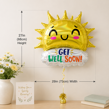 A gold foil sun-shaped balloon with a smiling face and a white cloud balloon reading 'GET WELL SOON!' in colorful letters, shown with dimension arrows indicating 27in height and 29in width on a tabletop with flowers and books nearby.