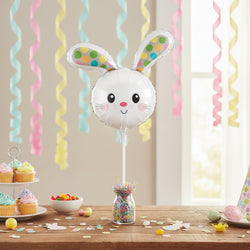 A white bunny-shaped foil balloon on a stick, featuring colorful polka-dot ears and a cute face, isolated on a white background.