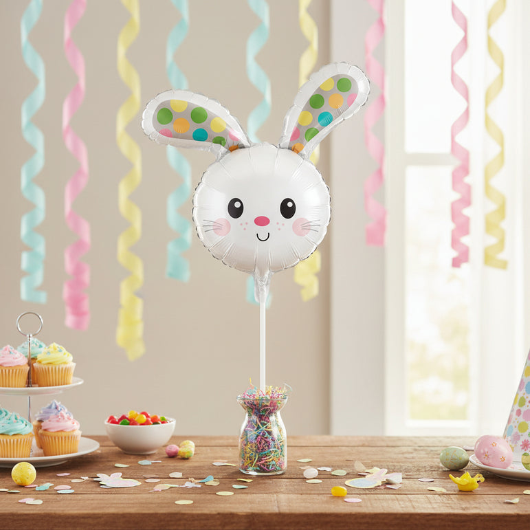 A white bunny-shaped foil balloon on a stick, featuring colorful polka-dot ears and a cute face, isolated on a white background.