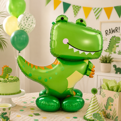 A large green dinosaur-shaped foil balloon stands on a decorated table in a party setting, with matching balloons, a cake, party hat, and printed boxes in a bright room.