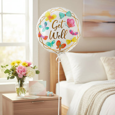 A round white foil balloon with scalloped edges, featuring the phrase 'Get Well' in gold script inside a gold geometric border, surrounded by colorful illustrated butterflies in yellow, teal, pink, orange, and purple on a white background.