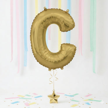 Gold letter 'C' balloon with a star-shaped weight against a pastel striped background