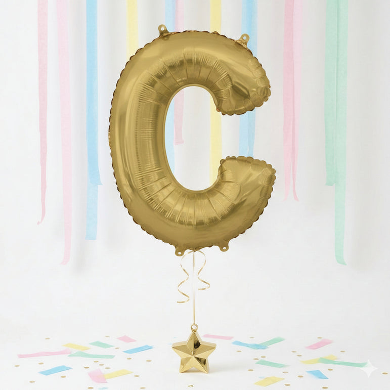 Gold letter 'C' balloon with a star-shaped weight against a pastel striped background