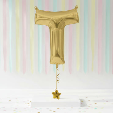 Gold foil balloon shaped like a letter 'T' with a star on a pastel striped background