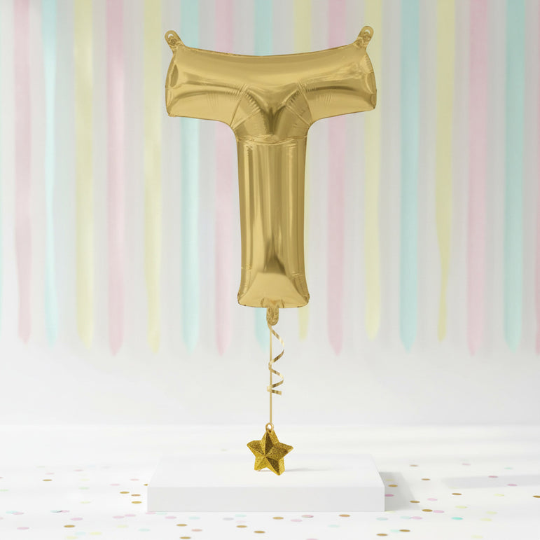 Gold foil balloon shaped like a letter 'T' with a star on a pastel striped background