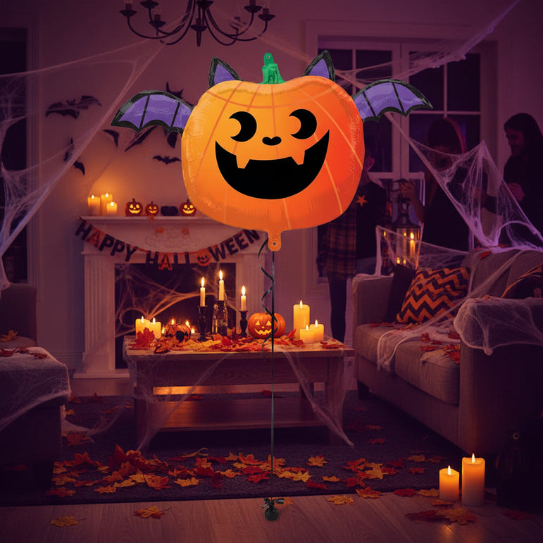 A Halloween pumpkin-shaped foil balloon with bat wings, featuring a carved jack-o'-lantern face and a green stem on a plain white background.
