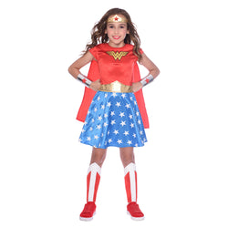 A girl dressed in a Child Wonder Woman Classic Costume with a red dress, blue skirt with white stars, white leg covers, red shoes, and a gold headband with the Wonder Woman logo.
